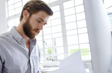 Photographie d'un homme lisant un document devant son ordinateur