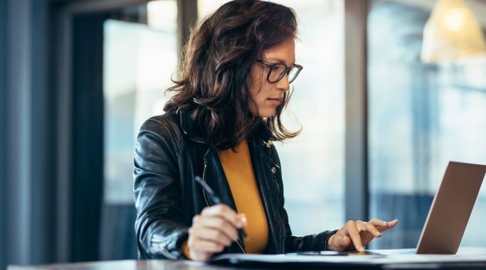 Femme affaires prenant des notes en regardant un ordinateur portable